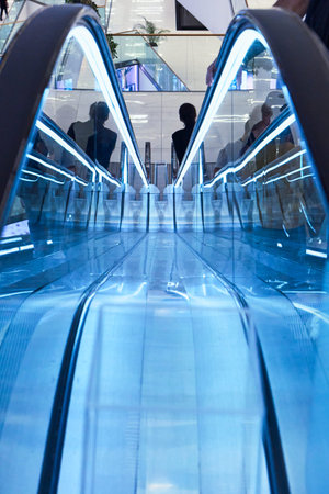 Brightly lit escalator features blue lighting in a busy shopping center.の写真素材