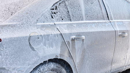 Water is sprayed on a silver sedan during a car wash activity outside. High quality photoの写真素材