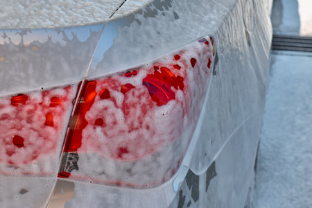 Water is sprayed on a silver sedan during a car wash activity outside. High quality photoの写真素材