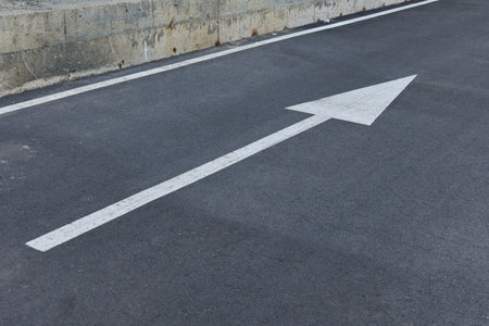 A large white arrow points straight ahead on a asphalt roadの写真素材