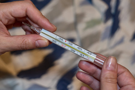A person holds a mercury thermometer measuring body temperature. High quality photo