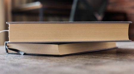 Stacked books resting on a wooden table indoors in a cozy environmentの写真素材
