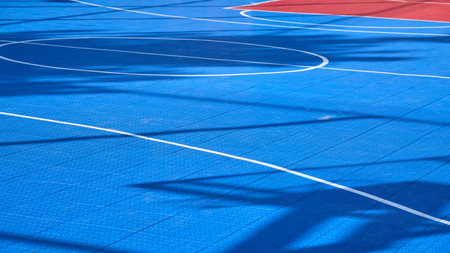 Vibrant blue basketball court shows shadows from treesの写真素材