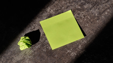 Green sticky note sits next to a crumpled paper ballの写真素材