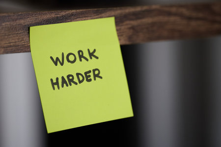 A sticky note with the words work harder is on woodの写真素材