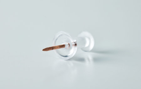 A single transparent map tack with a metal needle point, isolated on a light surface