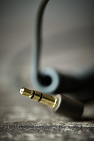 Macro shot of a gold-plated stereo mini-plug connector with a blurred cable on a textured surface