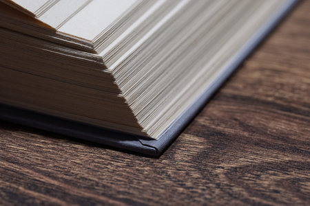 Macro shot of paper pages and book spine on a textured wooden desk, natural light, study mood