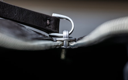 Close-up of a silver zipper slider with leather pull tab on a dark bag, shallow depth of field