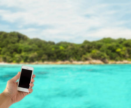 Close up of Male Hand Holding Smart Mobile Phone with Blank Screen on The Beach with Clear Sky used as Template to input Text or Photo, Business Conceptの写真素材