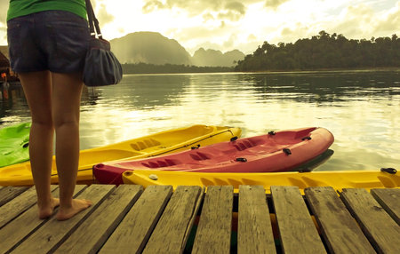 Vacation Start Here Concept, Soft Focus Color Filter Vintage Style Tone of Asian Woman Standing on The Wooden Pier at The Corner and Colorful Kayak in The River with Copyspace to input Textの写真素材
