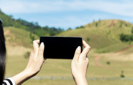 Close up of Female Hand Holding Smart Mobile Phone with Blank Screen with Mountain and Clear Sky of Ranong, Thailand in Background used as Template to input Text or Photo, Business Conceptの写真素材