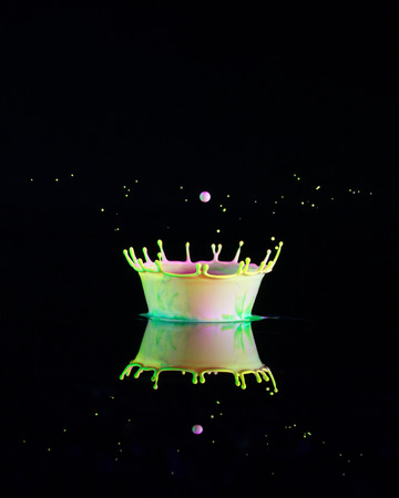 Liquid Drop Art - Water Drop Photography.  Water is dropped into coloured paint placed on a shiny black surface and forms a crown shape, which is reflected on the dark background.の写真素材