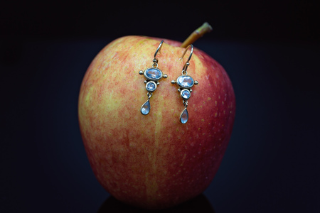 A pair of aquamarine gemstone earrings hooked into a red apple on a black backgroundの写真素材