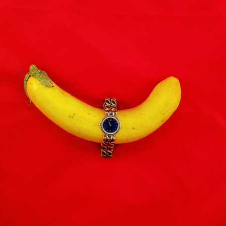 Vintage watch with black face encircling a yellow eggplant vegetable isolated on a red backgroundの写真素材