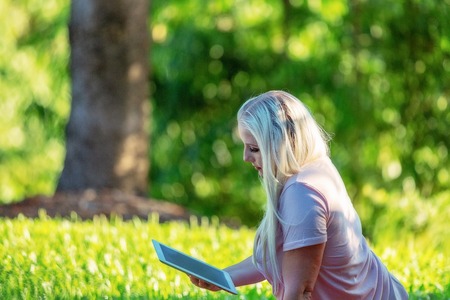 Young woman with long blond hair reading her computer tablet while relaxing in the gardenの写真素材