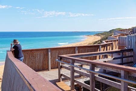 Female retiree on timber lookout taking photos of Logan's Beach whale nursery on The Great Ocean Road Australiaの写真素材