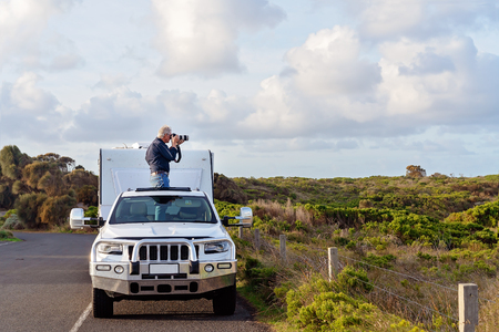 Male retiree on caravan holiday taking photos out of car sunroof on The Great Ocean Road Australiaの写真素材