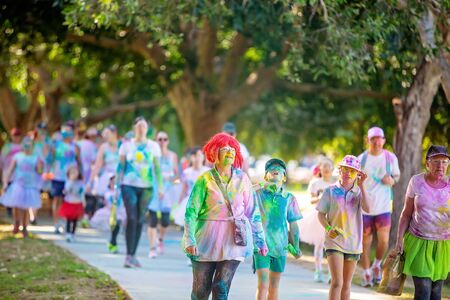 MACKAY, QUEENSLAND, AUSTRALIA - JUNE 2019: Unidentified senior woman in red wig splattered with colored powder walks with children and crowd in Color Frenzy Fun Runのeditorial素材