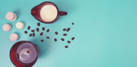 Red glass of black coffee and red jug of milk with marshmallows and scattered coffee beans, top view copy spaceの写真素材
