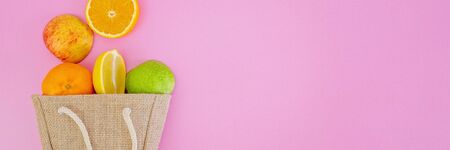 Fresh tropical citrus fruits in hessian shopping bag on pink background message card with copy space for textの写真素材