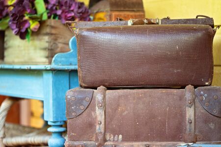 Two old leather suitcases stacked on top of each other in front of a blue table holding a box of flowersの写真素材