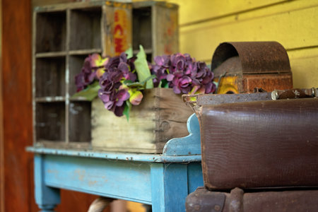 Two old leather suitcases stack on top of each other in front of a blue table holding a box of...