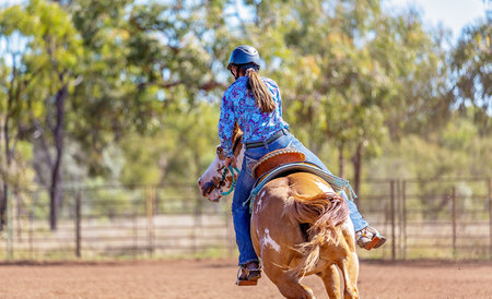Female equestrian competing in barrel racing in dusty arena at outback country rodeo