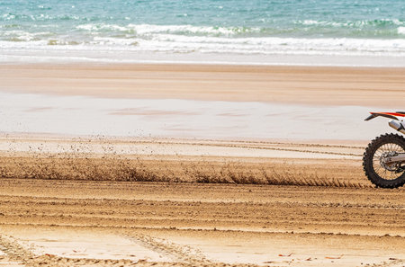 A close view of the blurred sand stirred up by a motorcyclist racing fast along the beach