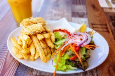 Salt and pepper calamari, chips and salad with freshly squeezed orange juice for lunchの写真素材
