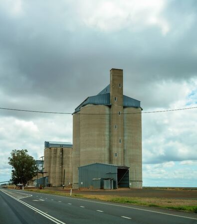 Grain storage silos by the side of the highway, with a stormy sky in the backgroundの写真素材