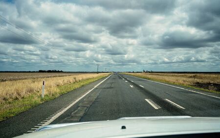 A long straight Australian highway with storm clouds gathering, as seen through a car windscreenの写真素材