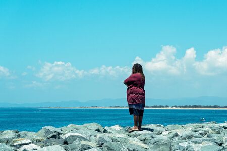 Mackay, Queensland, Australia - October 2019: A Thursday Islander native man with dreadlocks standing on rocks at the harbour wall looking out to sea on a summery dayのeditorial素材