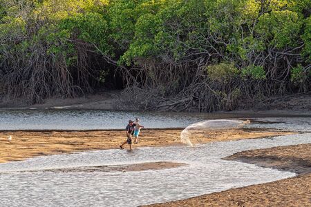 Mackay, Queensland, Australia - October 2019: A man and child casting a net in a creek at low tide to catch bait to go fishing against a mangrove backdropのeditorial素材