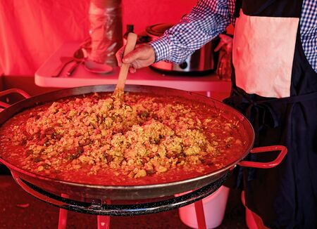 Man stirring a large pan of bubbling hot and delicious savory paella at a market stallの写真素材