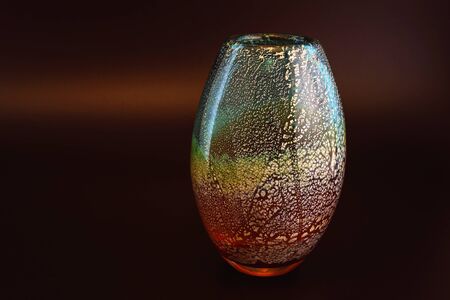 Hand blown colourful and decorative glass vase threaded with gold isolated against a dark backgroundの写真素材