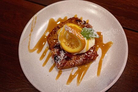 A slice of carrot and raisin loaf topped with yoghurt and an orange slice, with mint leaf garnishの写真素材