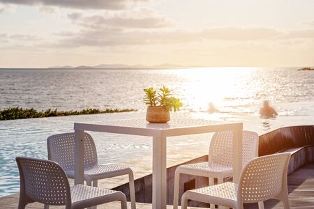 Outdoor table and chairs beside an infinity edge lagoon bathed in soft early morning light from across the ocean, a peaceful vista in Australia. Swimmer in the background.の写真素材