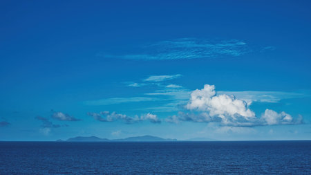 A creative imaginative cerulean sky with a white fluffy clouds over water and islands on the...