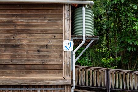 A weathered slat timber wall of a bushland toilet building with raised water tank and sign that pets are allowedの写真素材