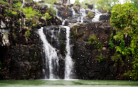 Rain drops falling in front of an intentionally blurred Cedar Creek Falls in North Queensland in the...