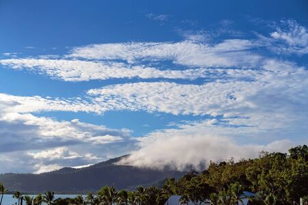 Beautiful cloud formation in the blue sky and misty over the mountains at a tropical seaside resort in early morning lightの写真素材