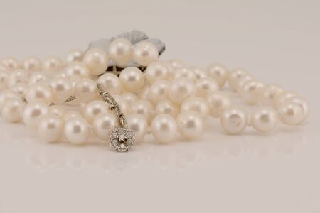A flower design diamond and white gold pendant nestled in front of lustrous pearls, isolated on a white backgroundの写真素材