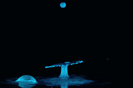 Two blue water droplets collide and form an umbrella shape with another coming down from above and...