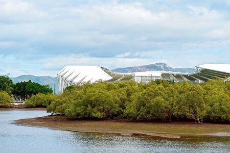 A new and modern all purpose stadium building behind mangrove trees on the river bankの写真素材