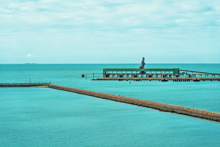 Industrial wharf with ship loading facilities beside a marina stone wall in a wide blue oceanの写真素材