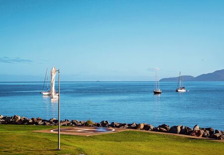 Yachts anchored off shore near a helicopter landing pad on a beautiful clear calm day on the oceanの写真素材