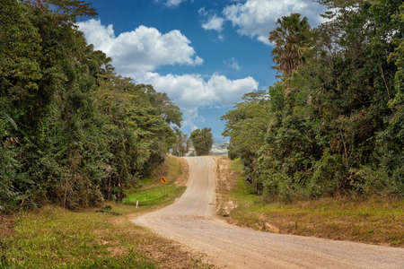 A country dirt road leading over a hill with an arrow sign indicating a winding road in the distanceの写真素材