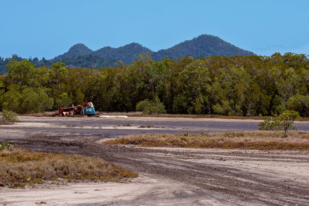 A rusting car wreck on a tidal salt pan environment with tire tracks in the mud