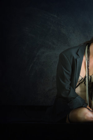 Woman posing for boudoir photograph in intimate clothing and jacket against a black textured...